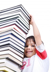 A big tower of many books vertical and kid reaching a top